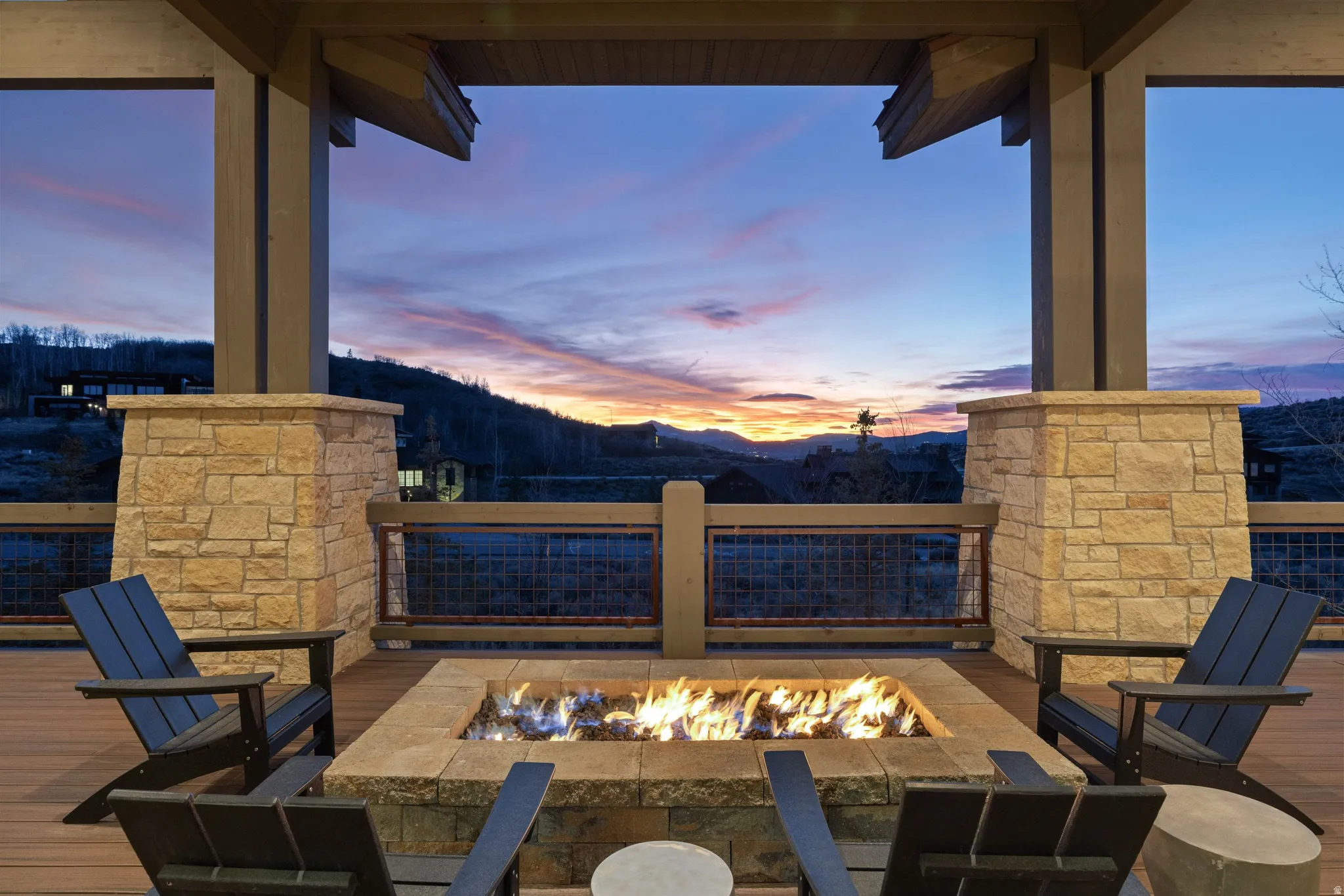 Covered outdoor deck with a built-in stone fire pit, wood-finish flooring, and stone pillars