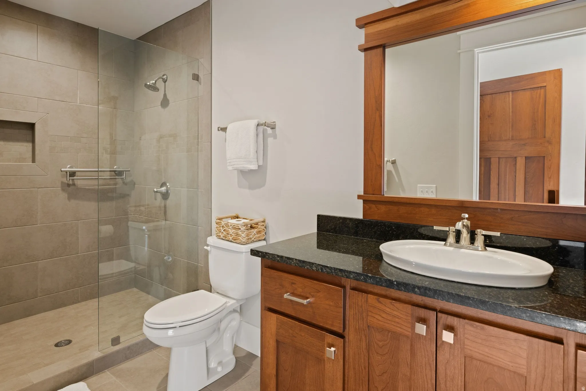 Bathroom featuring a glass-enclosed shower with tiled walls and a recessed niche, wood-finish vanity with a dark countertop, white oval vessel sink, and a framed mirror