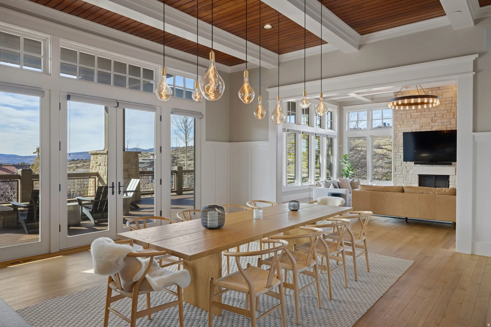 Spacious open-concept interior featuring light wood-finish flooring, a coffered ceiling with wood paneling, and an array of pendant lighting fixtures