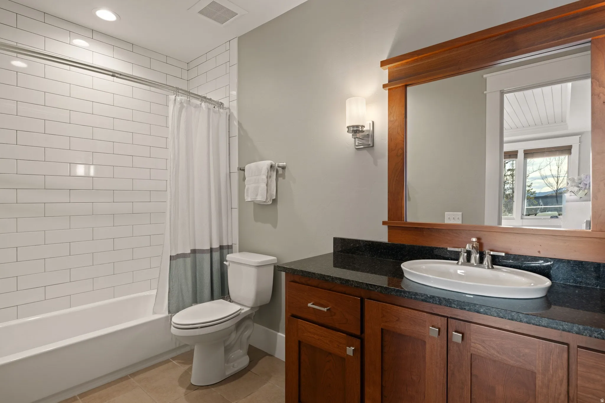 Bathroom featuring a tub/shower combination with white subway tile surround, a built-in wood-finish vanity with dark countertop, an oval undermount sink, and a framed mirror