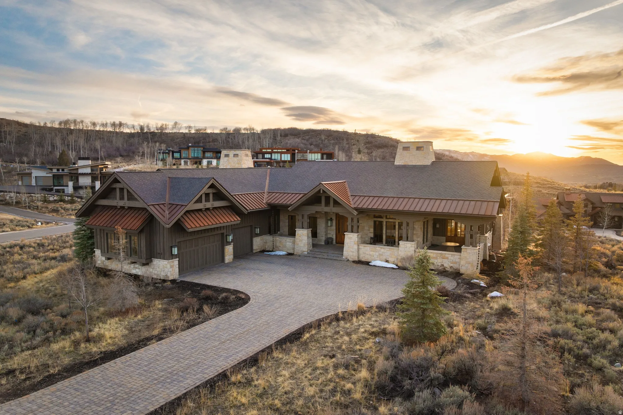 Contemporary mountain residence featuring a stone and wood facade, a paver driveway, and a multi-gabled roofline with copper accents
