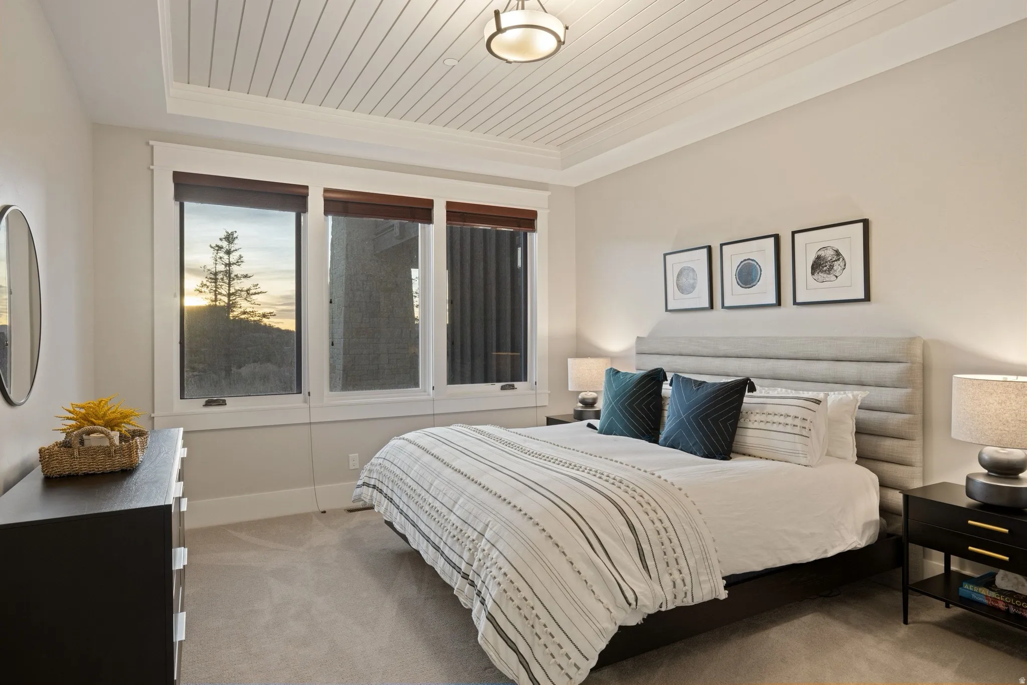 Carpeted bedroom featuring a tray ceiling with wood-finish paneling, three large windows, and an upholstered headboard