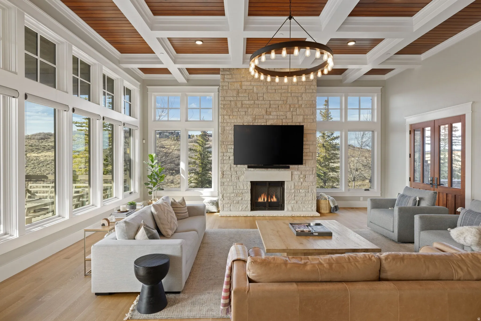 Spacious living area featuring a stone fireplace, wood-finish flooring, and a coffered ceiling with wood paneling