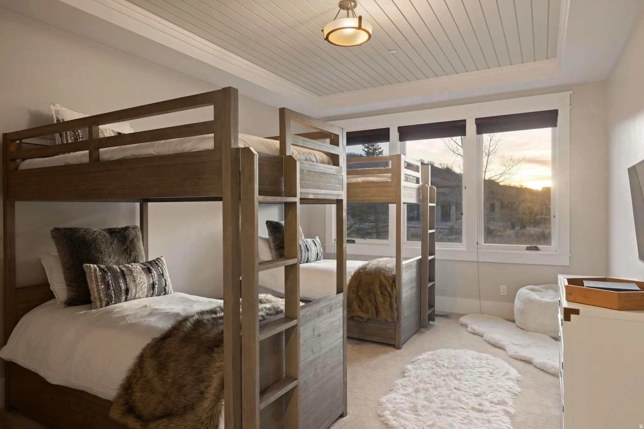 Room with two wooden bunk beds, white walls, and a planked ceiling
