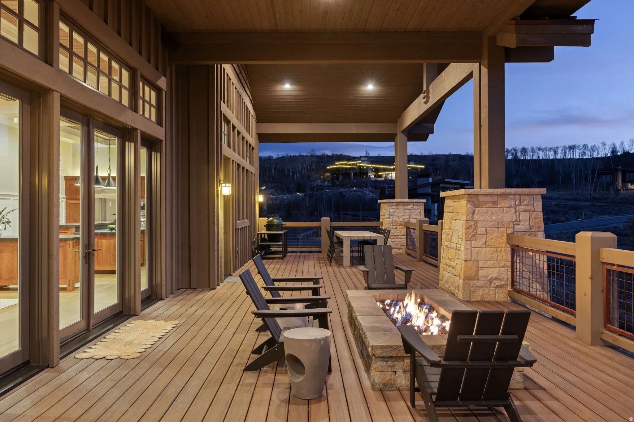 Expansive outdoor deck featuring a built-in stone fire pit, wood-finish flooring, and stone-clad support columns