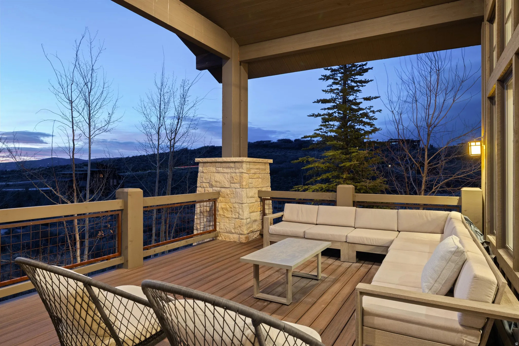 Covered outdoor deck featuring wood-finish flooring, a stone-clad pillar, and a railing with metal infill