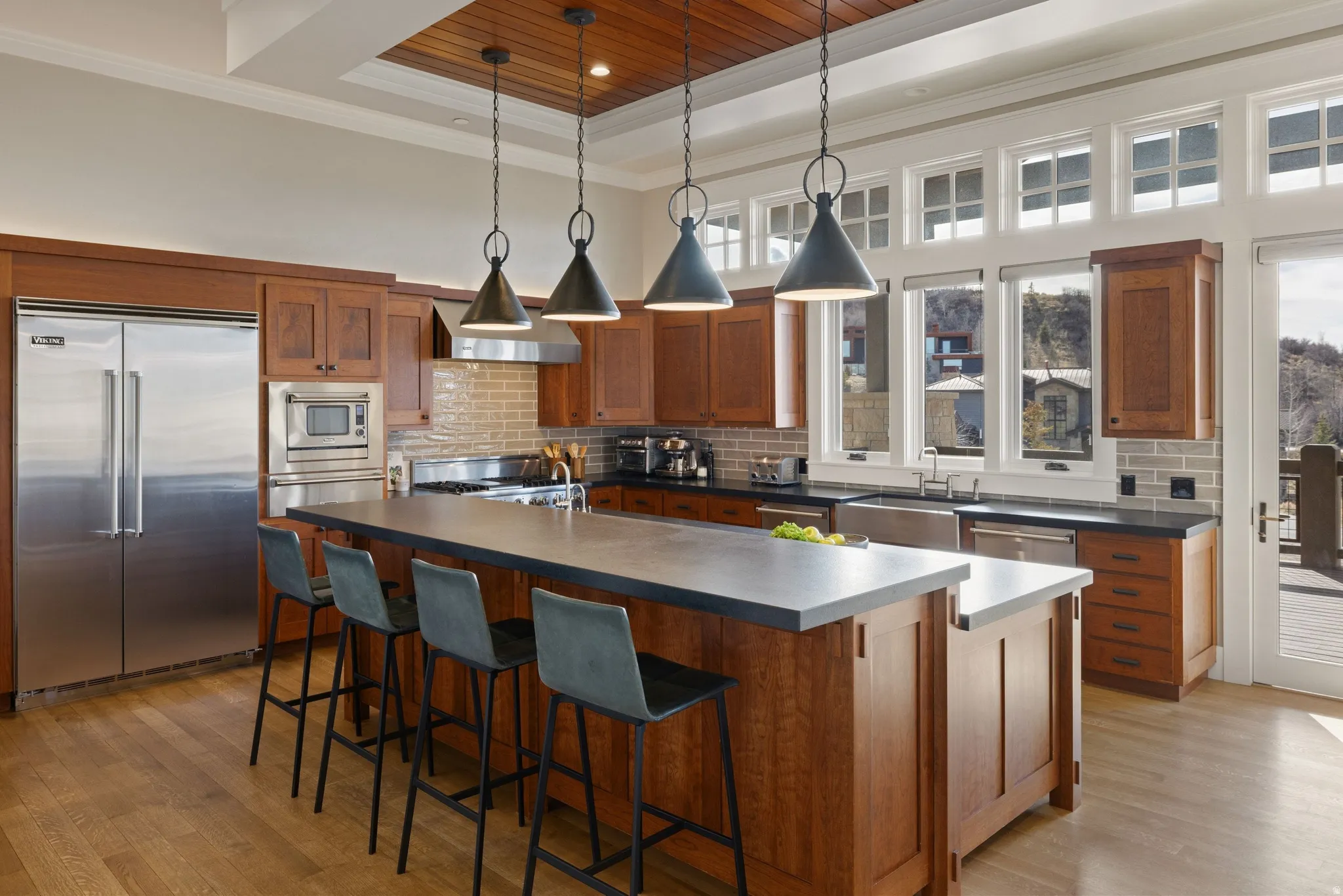 Gourmet kitchen featuring a wood-finish coffered ceiling, hardwood flooring, stainless steel appliances, a large island with seating, and extensive cabinetry