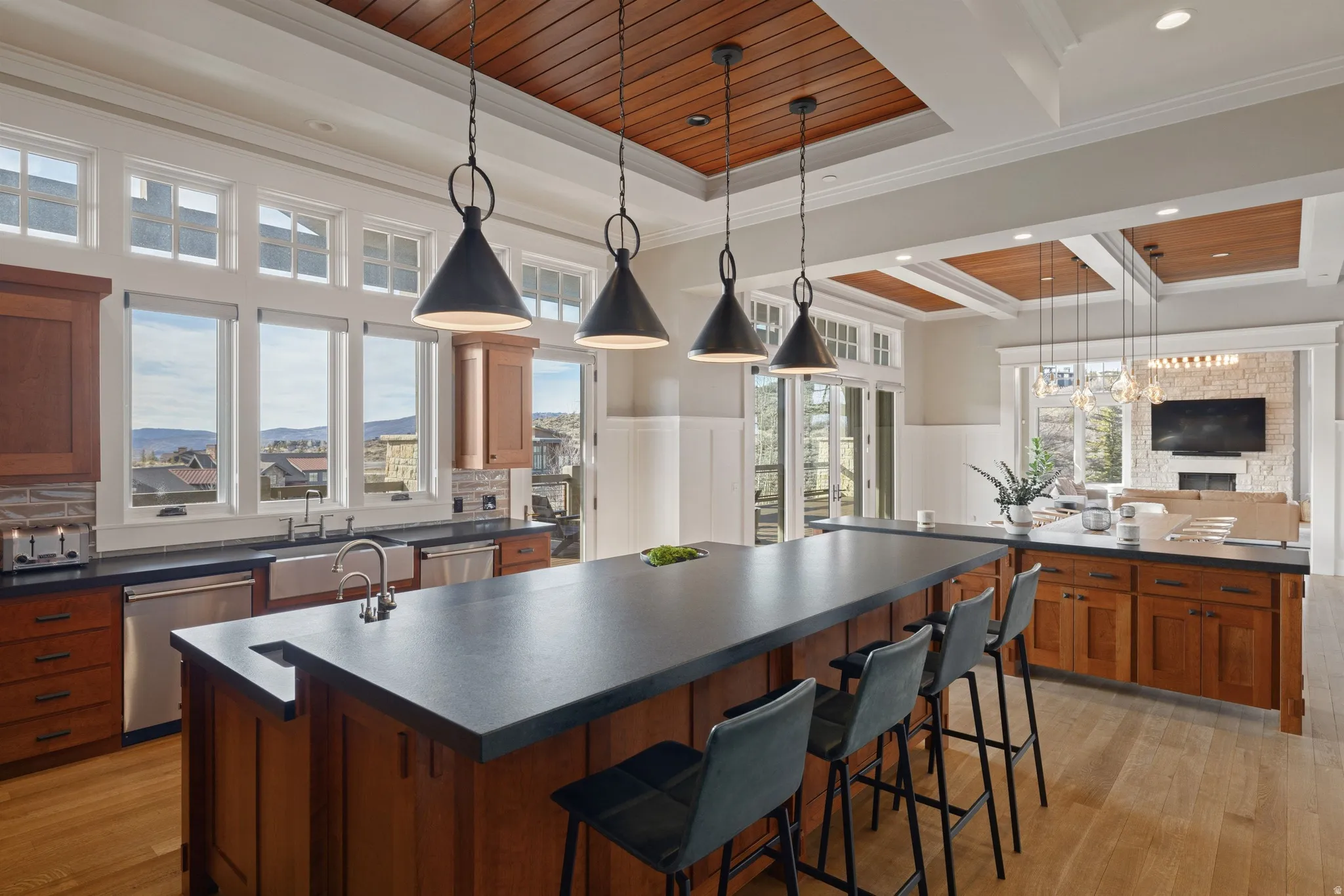 Open-concept kitchen featuring an expansive center island with seating, dark countertops, wood-finish flooring, and recessed wooden ceiling panels