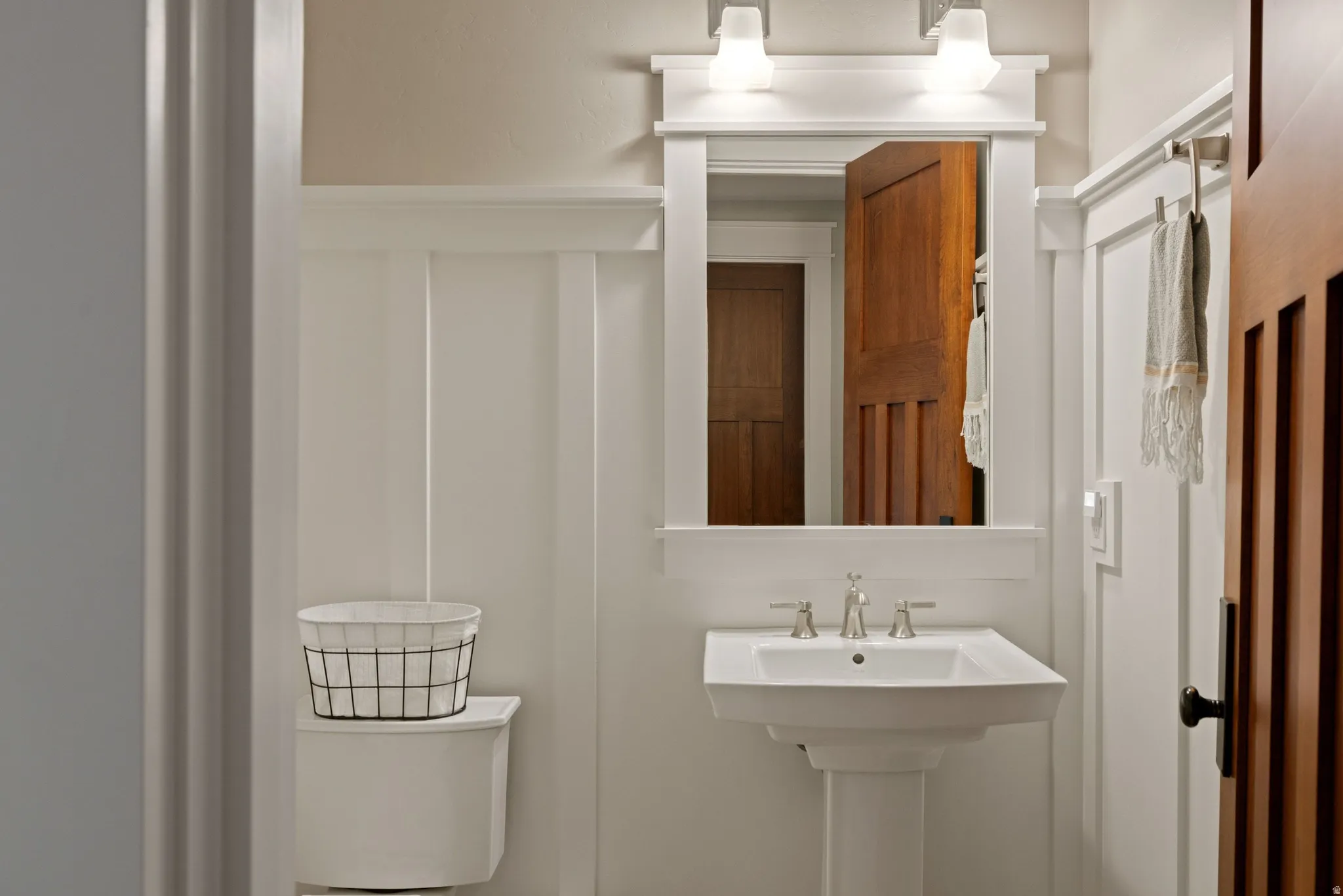 Bathroom featuring a pedestal sink with a chrome faucet, wall-mounted mirror, and overhead sconce lighting
