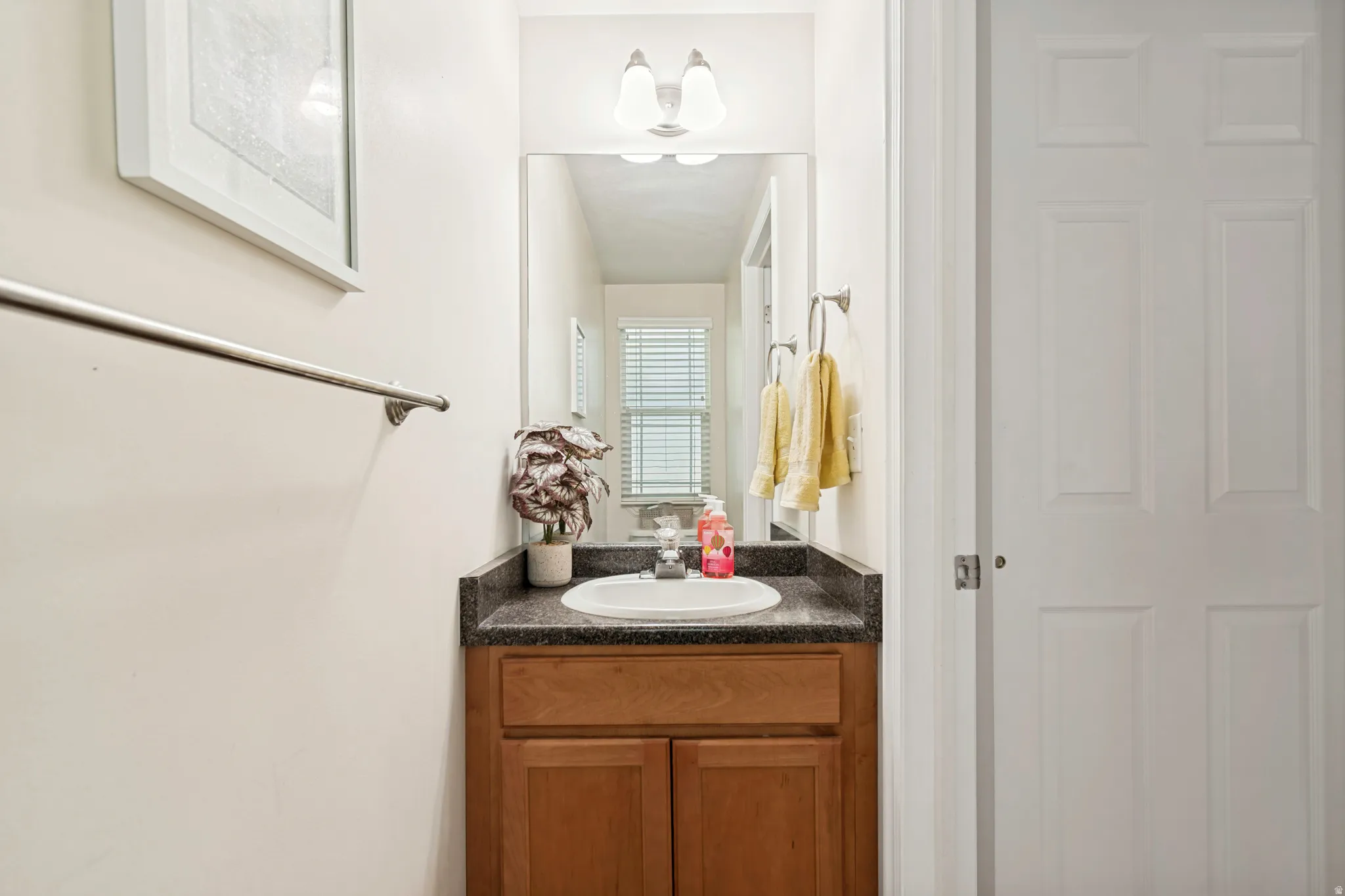 Bathroom vanity featuring a wood-finish cabinet, a dark countertop, an integrated sink, and a wall-mounted mirror