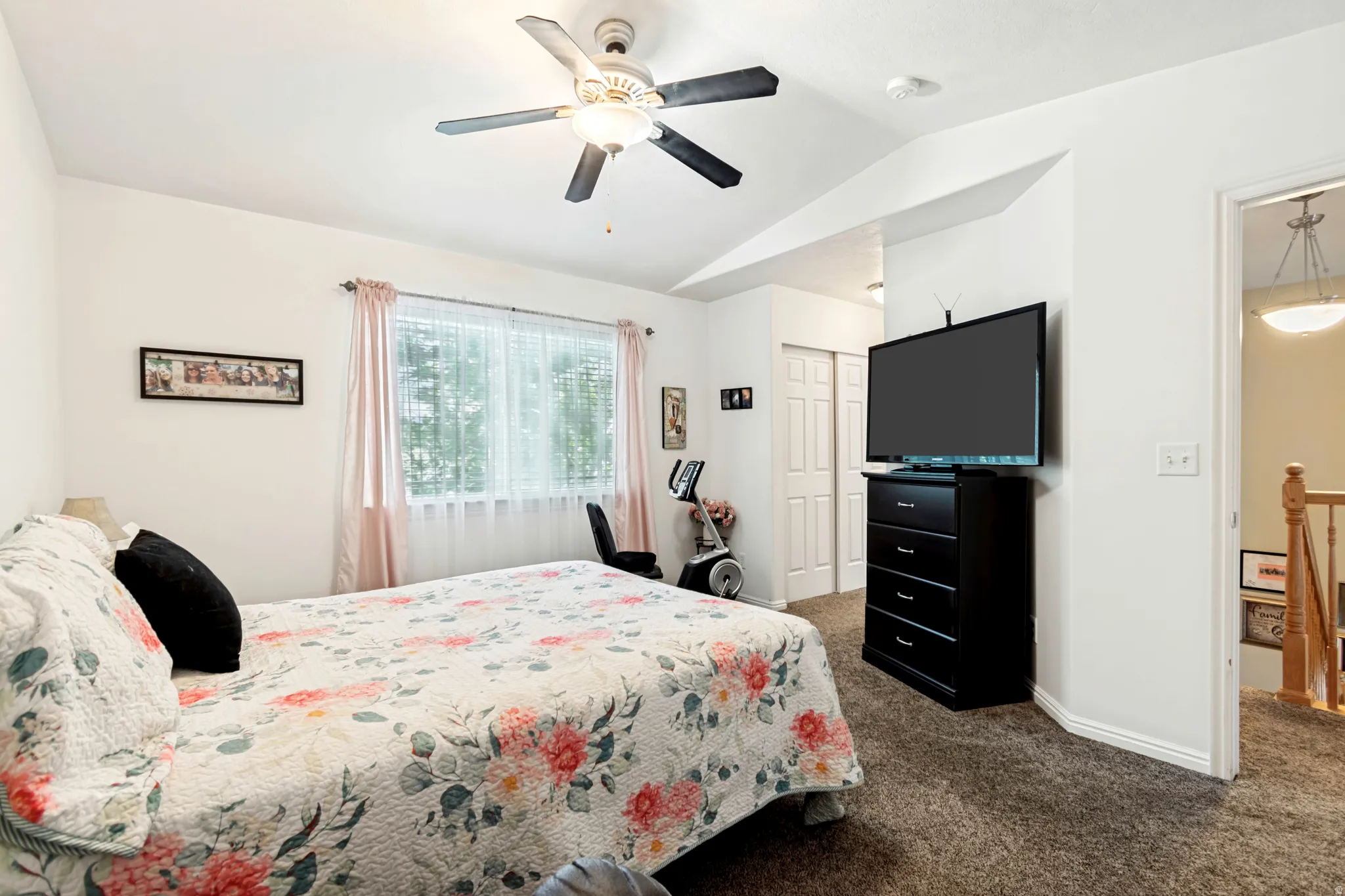 Carpeted room featuring a ceiling fan, vaulted ceiling, and a window with blinds and drapes