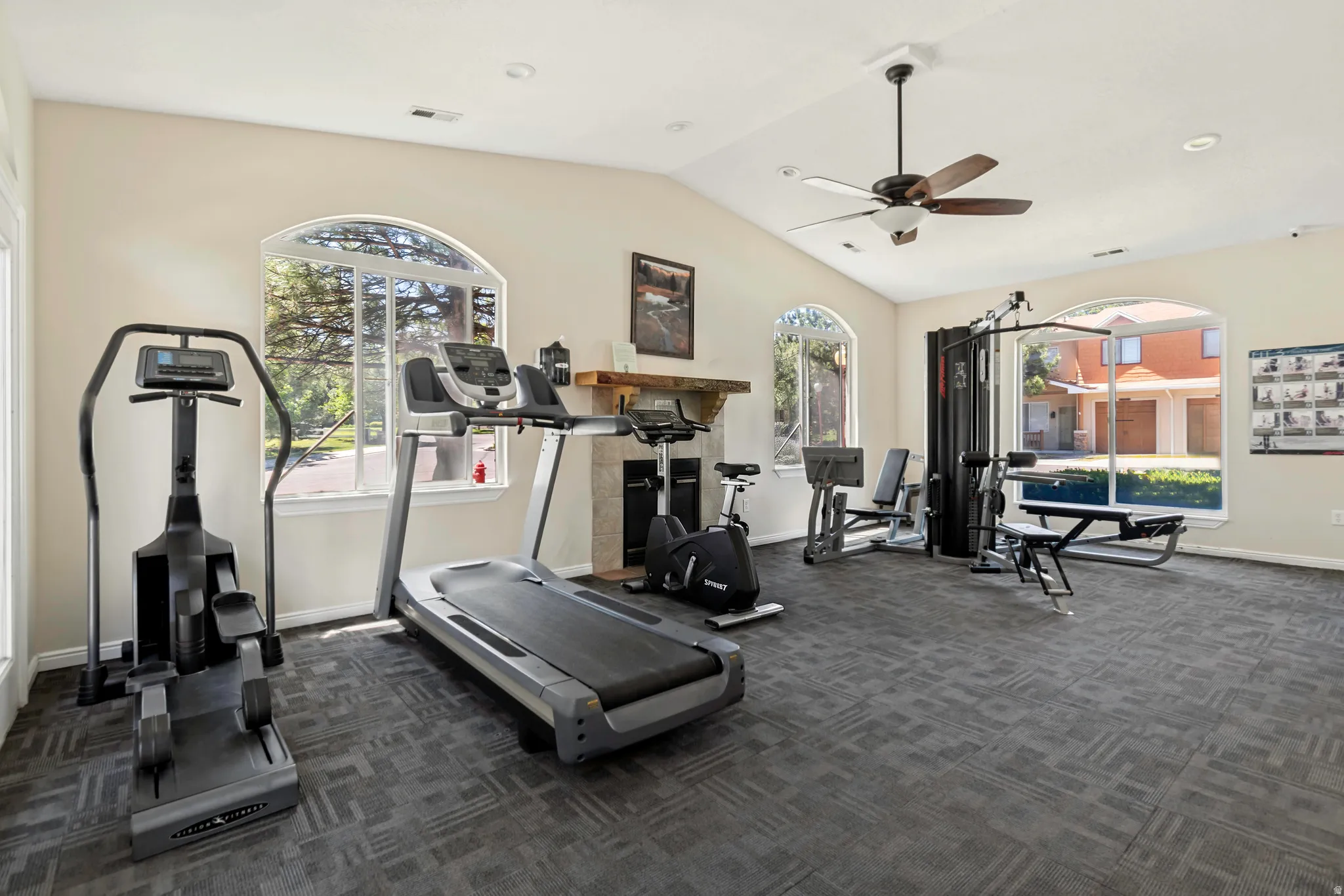 Spacious room with vaulted ceilings and a ceiling fan, featuring carpet tile flooring