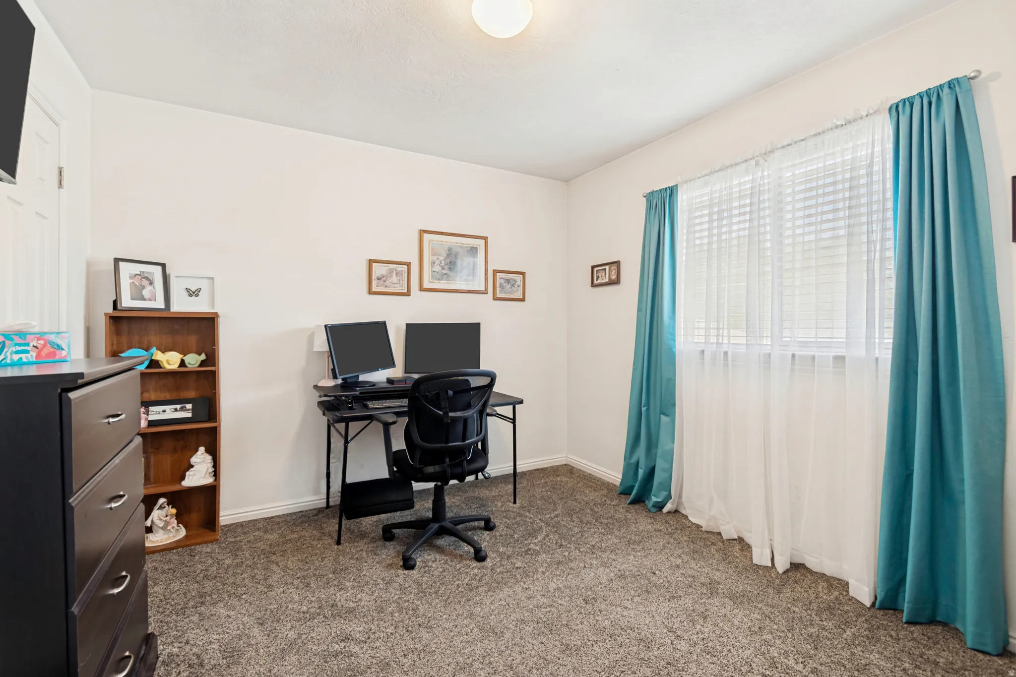 Light-filled room featuring a single window with blinds and full-length drapes, neutral wall paint, and gray carpet flooring