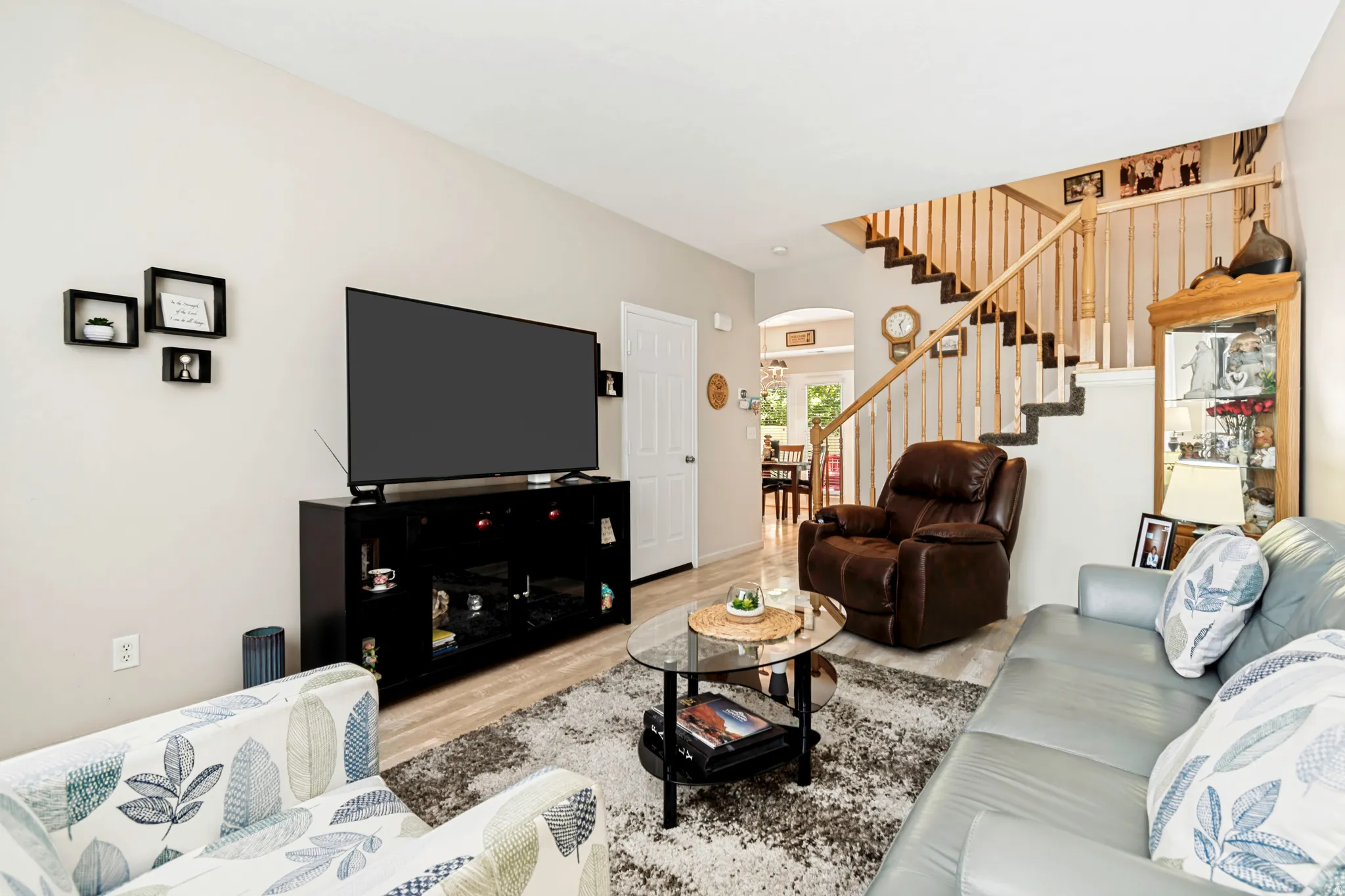Living area featuring light-toned walls, wood-finish flooring, and a staircase with natural wood banisters