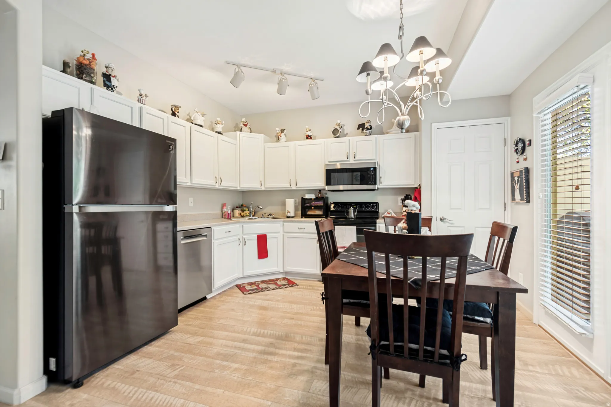 Kitchen featuring white cabinetry with brushed nickel hardware, stainless steel appliances, wood-finish flooring, a white track lighting fixture, and a white chandelier