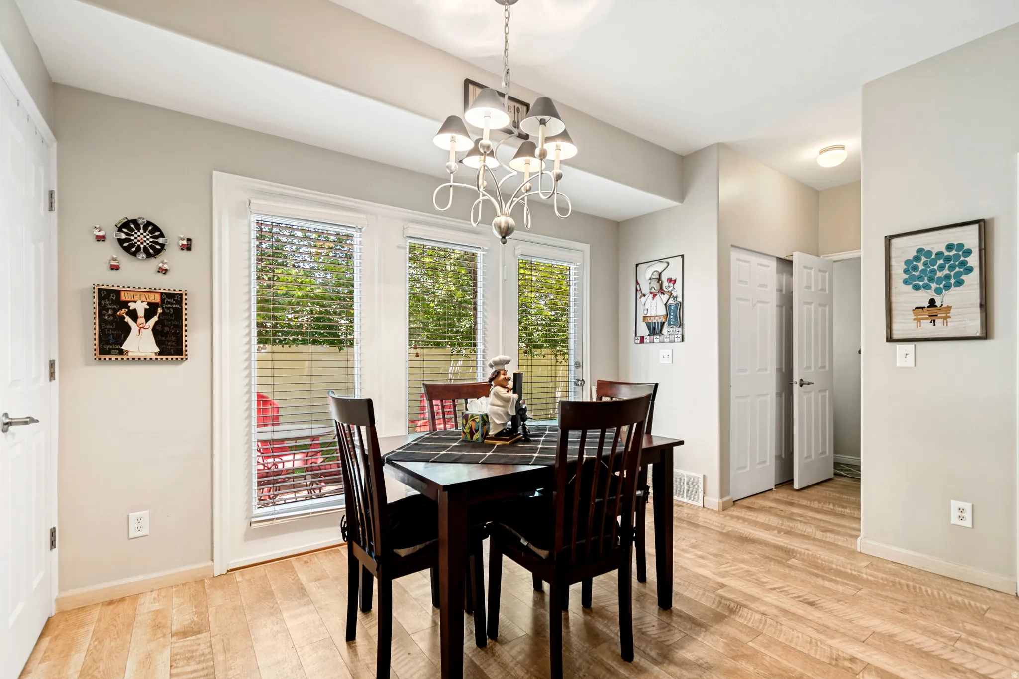 Dining area featuring wood-finish flooring, a contemporary chandelier, and a wall of windows offering natural light