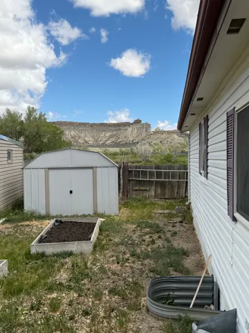 Expansive property featuring a metal storage shed, raised garden beds, and a prominent cliffside backdrop