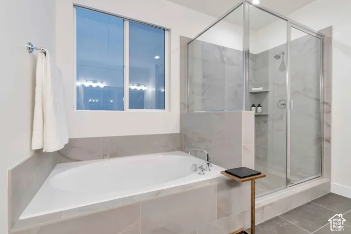 Soaking tub with chrome faucet, glass-enclosed shower with tiled surround, and large-format tile flooring