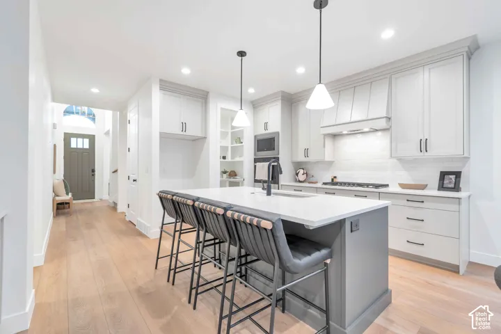 Kitchen featuring white shaker-style cabinetry, a contrasting center island with a stone countertop, built-in stainless steel appliances, wood-finish flooring, and pendant lighting