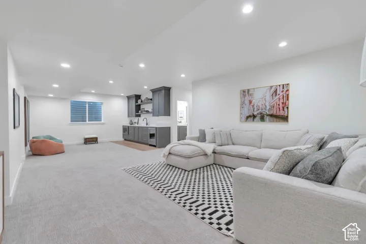 Open-concept interior featuring wall-to-wall carpeting, recessed ceiling lighting, and a kitchenette with dark-toned cabinetry, a built-in microwave, and a beverage refrigerator