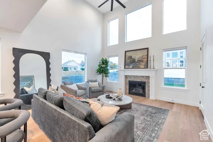 Living area featuring a vaulted ceiling, floor-to-ceiling windows, gas fireplace with a decorative tile surround, wood-finish flooring, and a ceiling fan