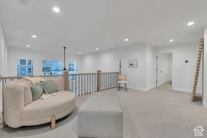 Open-concept loft area featuring neutral wall-to-wall carpeting, recessed ceiling lighting, and a metal-and-wood spindle railing