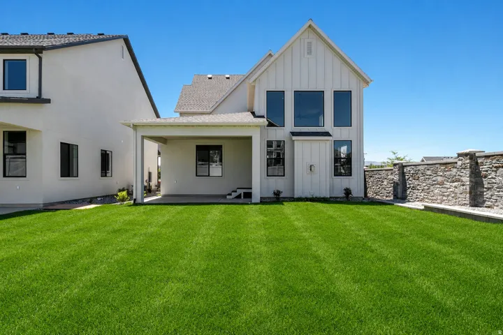Spacious rear yard with a manicured lawn, covered patio, and stone retaining wall