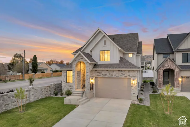 Two-story exterior featuring a stone and board-and-batten facade, arched entryway, concrete driveway, and stone perimeter wall