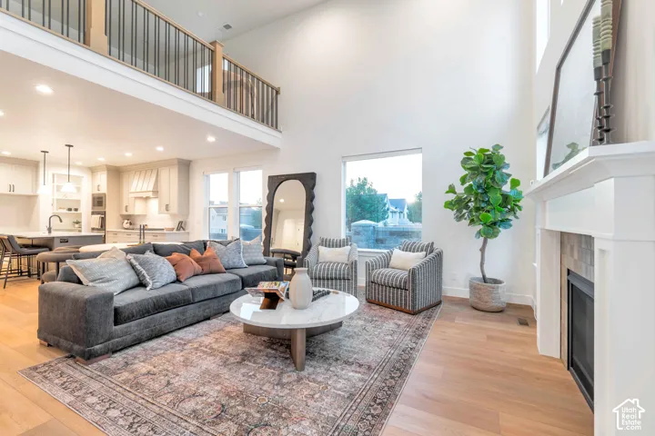 Double-height ceiling, open-plan layout featuring wood-finish flooring, fireplace with a mantle, mezzanine level with metal spindle railings, and recessed lighting