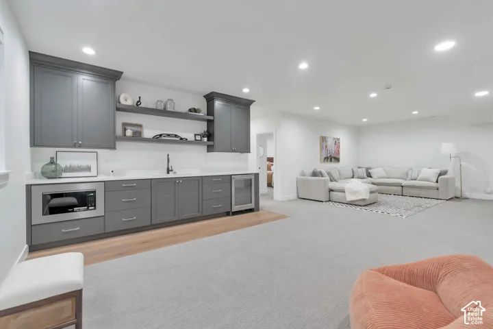 Wet bar featuring gray shaker-style cabinetry, quartz countertops, open shelving, integrated microwave, and beverage refrigerator with recessed lighting throughout