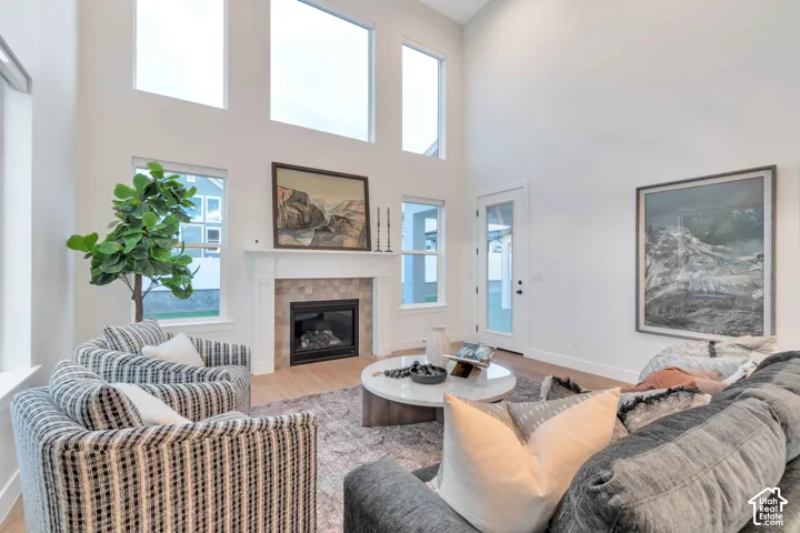 Vaulted ceilings with oversized windows, fireplace with a tile surround and mantel, wood-finish flooring, and glass-paneled exterior door