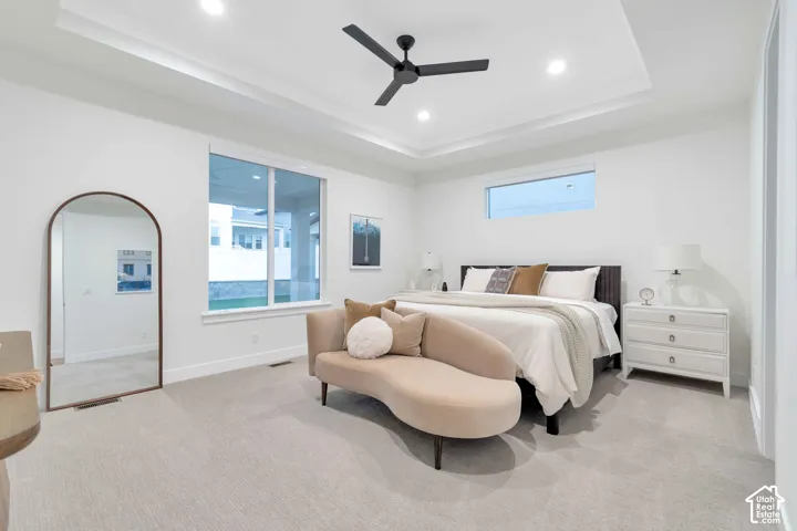 Tray ceiling featuring recessed lighting and a matte black ceiling fan, complemented by large windows, neutral carpeting, and crisp white wall finishes