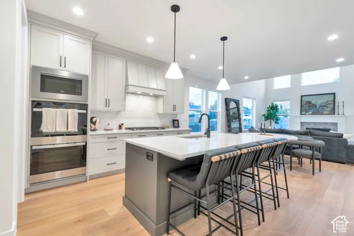Kitchen featuring light-colored cabinetry, stone-finish countertops, stainless steel wall-mounted oven and microwave, central island with an undermount sink, and wood-finish flooring