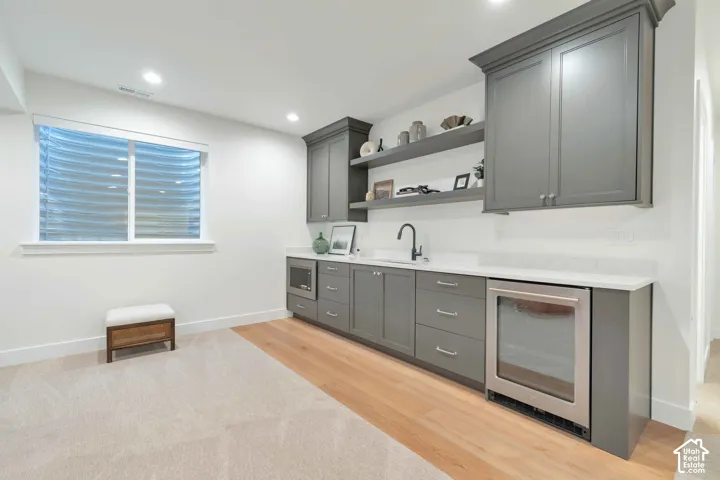 Wet bar featuring custom dark gray cabinetry, quartz countertops, integrated stainless steel beverage refrigerator, built-in microwave, and matte black faucet