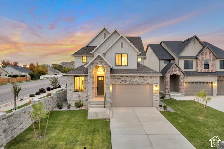 Multi-level exterior featuring vertical siding, stone masonry accents, an arched covered entryway, a concrete driveway, and a stone retaining wall