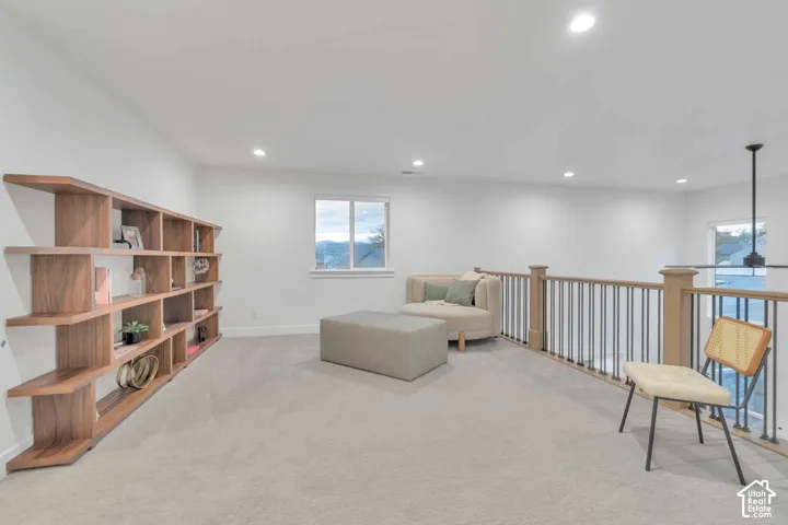 Open-concept area featuring recessed lighting, wall-to-wall carpeting, a floor-to-ceiling built-in wood shelving unit, and a railing with metal balusters
