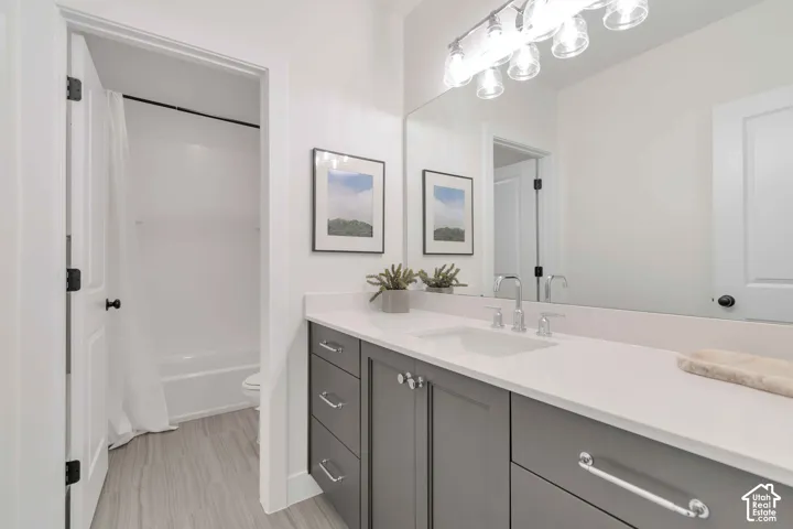Bathroom featuring a grey vanity with white solid-surface countertop, rectangular undermount sink, expansive wall-mounted mirror, and multi-bulb polished chrome vanity lighting