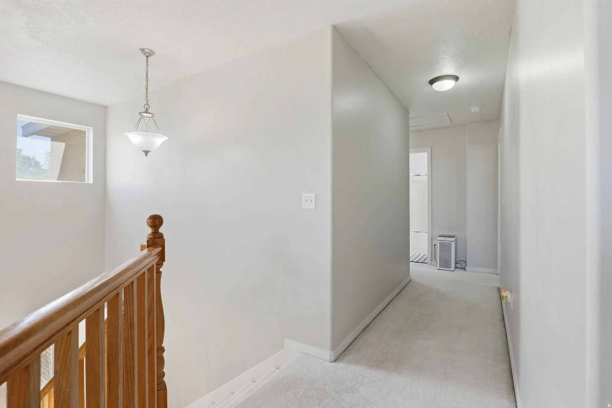 Upper landing featuring a wood handrail, spindle newel post, and a decorative pendant light fixture
