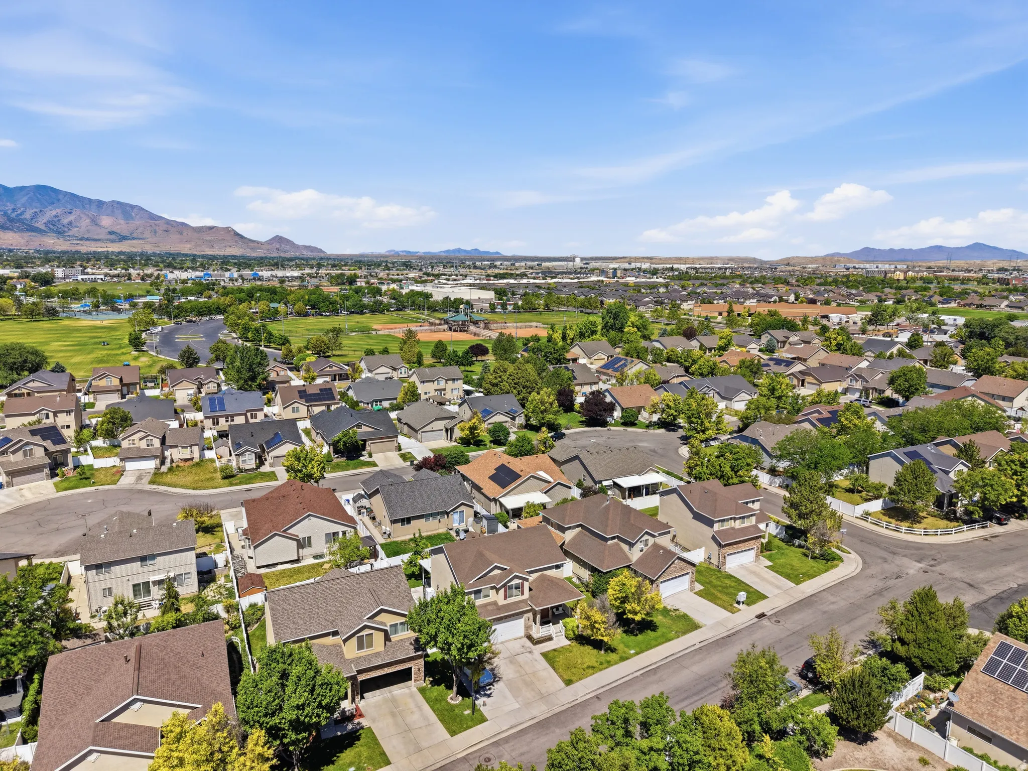 Aerial perspective showcasing a residential area with varied home styles, several properties featuring rooftop solar panels, green spaces, and distant mountains