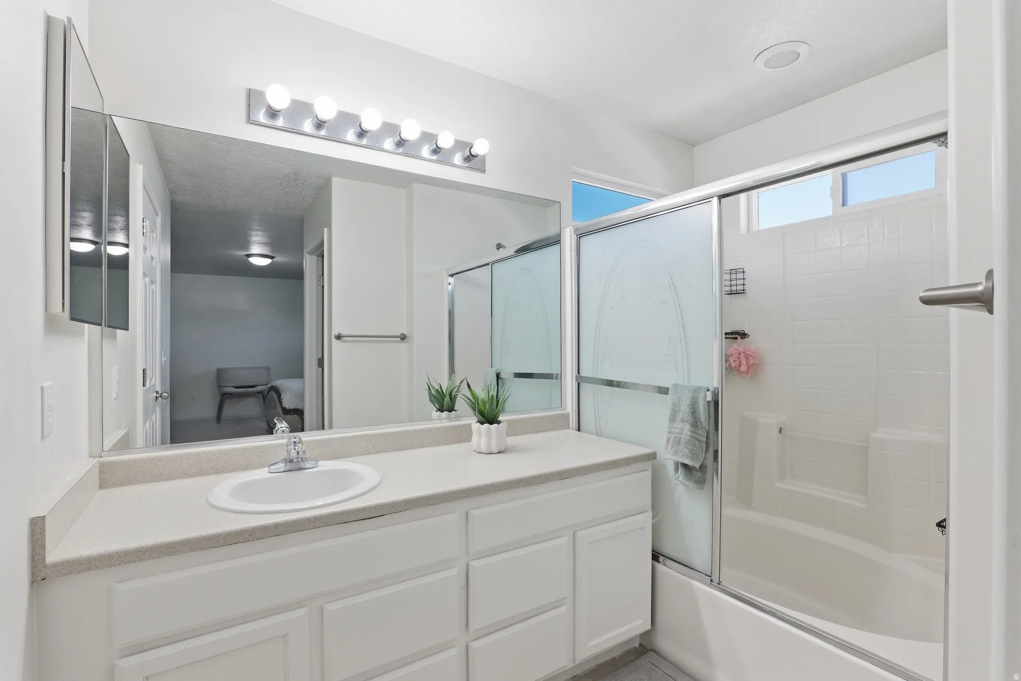 Bathroom featuring a white vanity with an integrated sink, a large wall-mounted mirror, and overhead vanity lighting