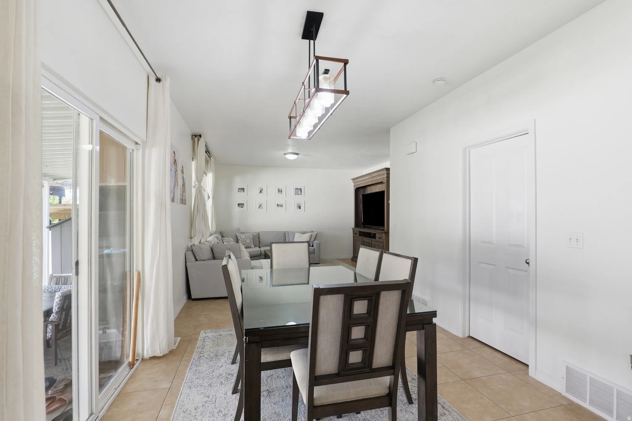 Bright dining area featuring tile flooring, a contemporary linear chandelier, and access to an outdoor space via a sliding glass door