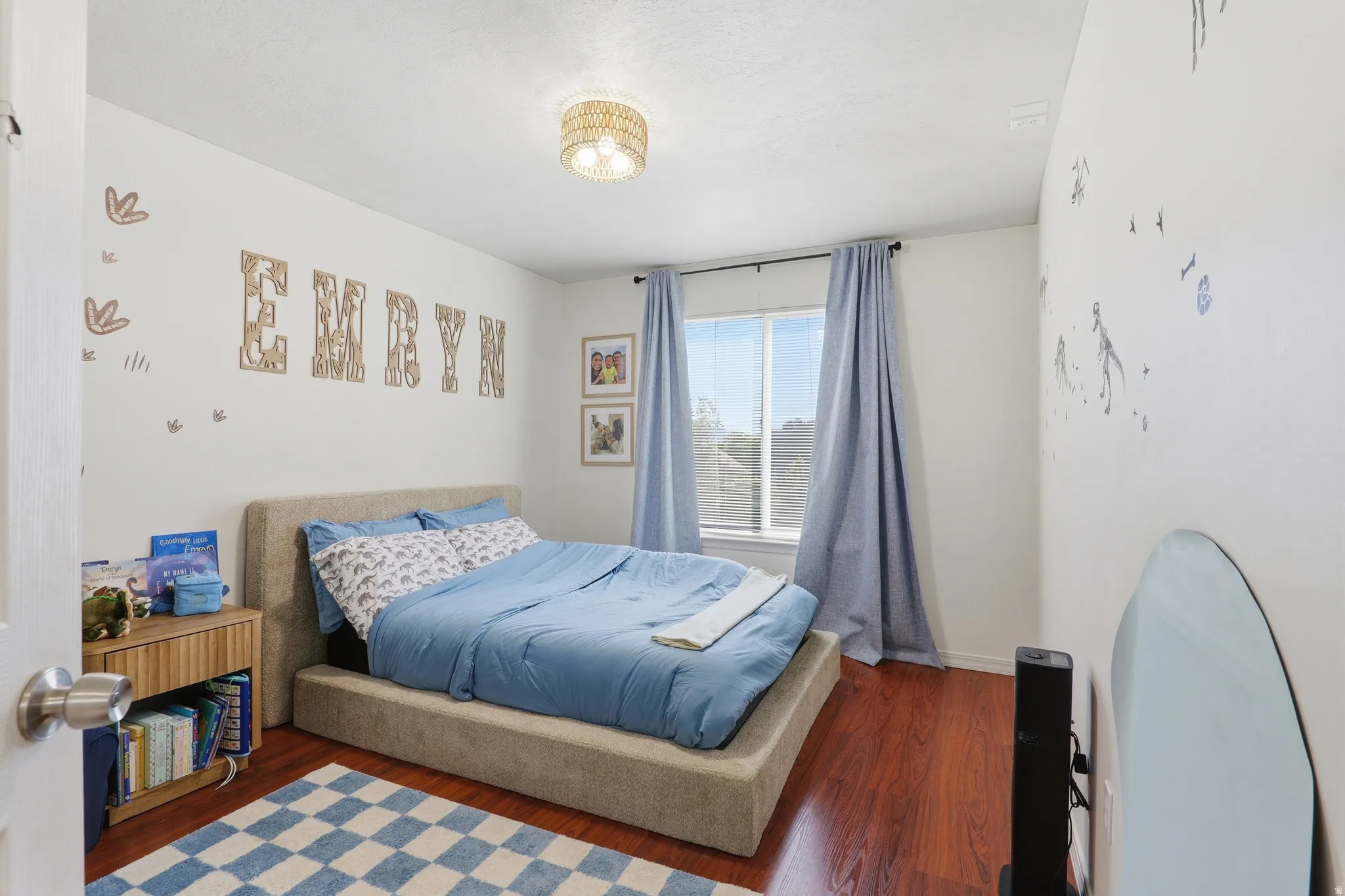Bedroom featuring wood-finish flooring, a contemporary ceiling light fixture, a single window with curtain rods, and a white interior door with brushed nickel hardware