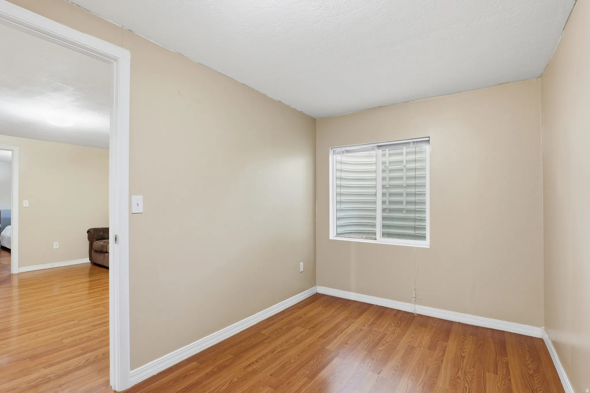 Room with wood-finish flooring, neutral wall paint, white baseboards, and a window with horizontal blinds
