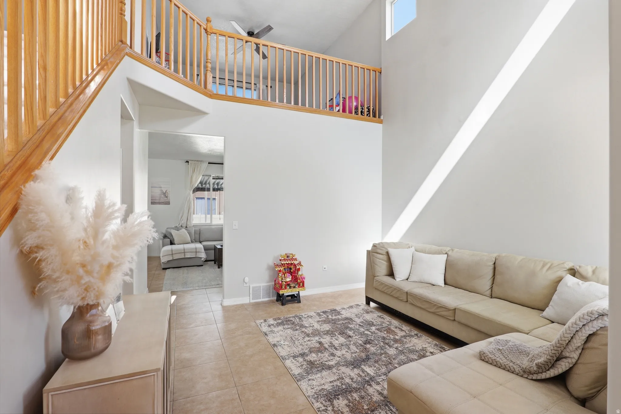 Two-story living area featuring a wood-finish staircase with balusters, a second-story landing overlooking the space, a ceiling fan, and tile flooring