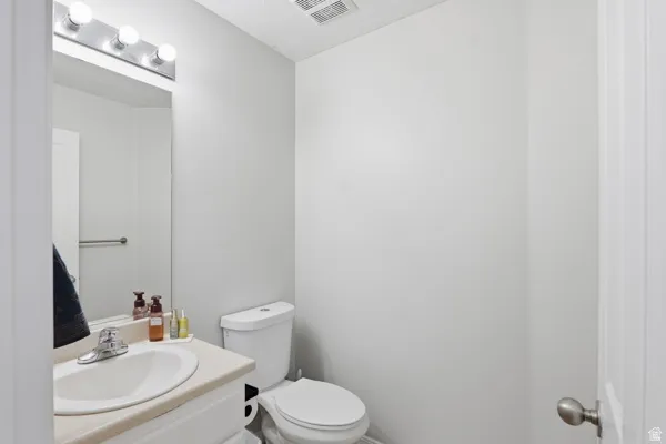 Compact bathroom featuring a single-basin vanity with a laminate countertop, a chrome faucet, and a wall-mounted mirror with overhead bar lighting