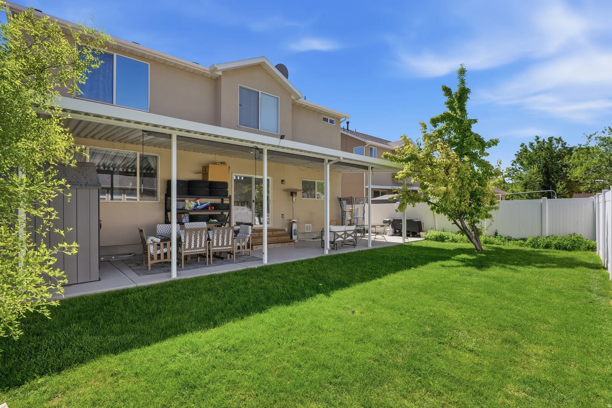 Expansive backyard featuring a large concrete patio with a full-length covered awning, mature trees, and a white privacy fence