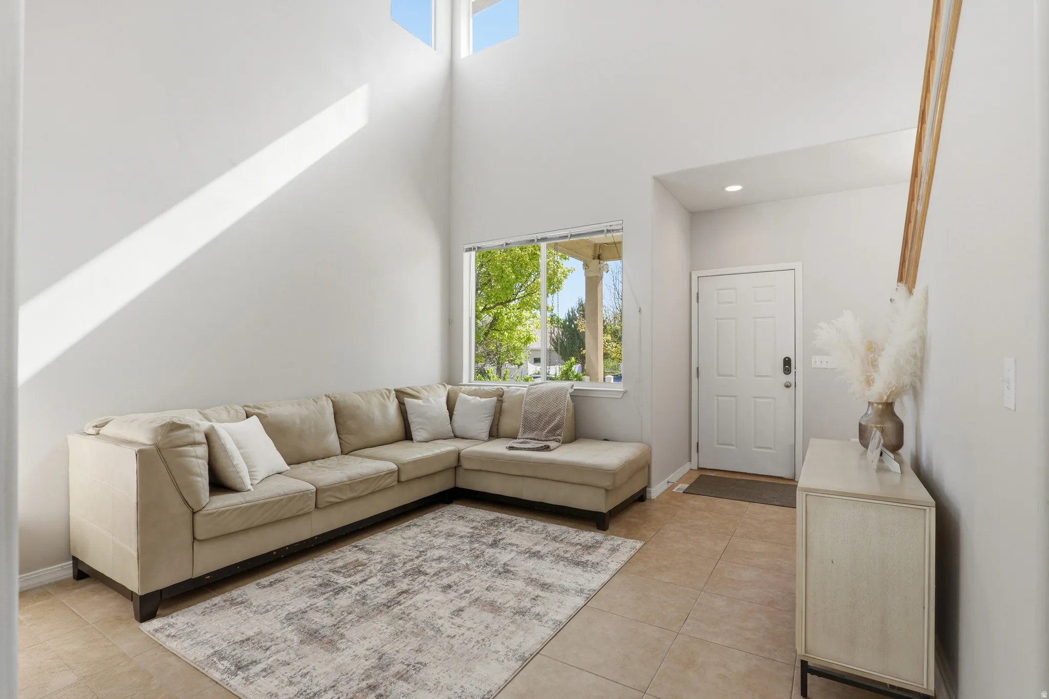 Foyer featuring vaulted ceilings, a prominent window, a paneled entry door, and light-toned tile flooring