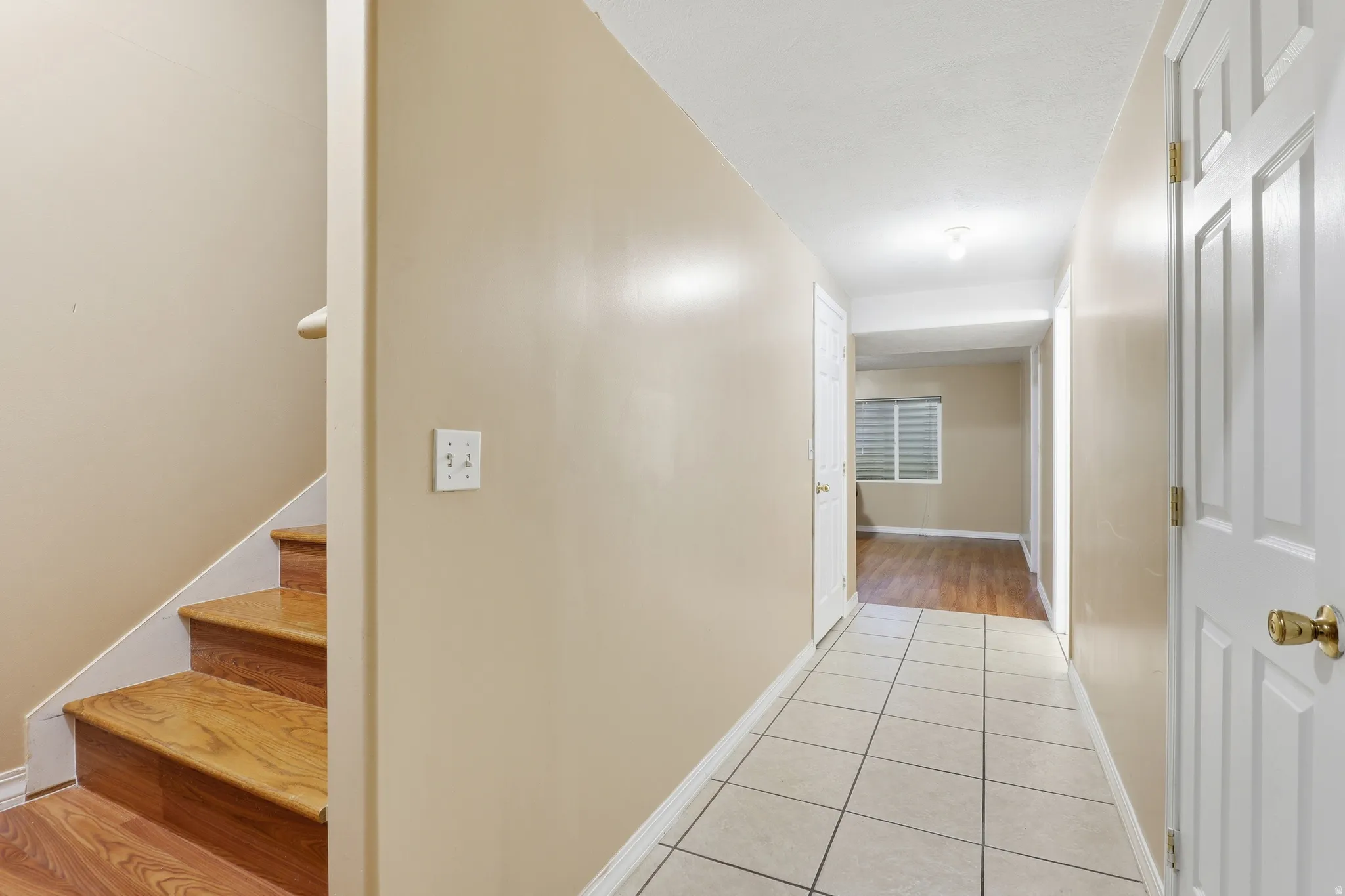 Tiled entryway with wood-finish flooring extending into the background room