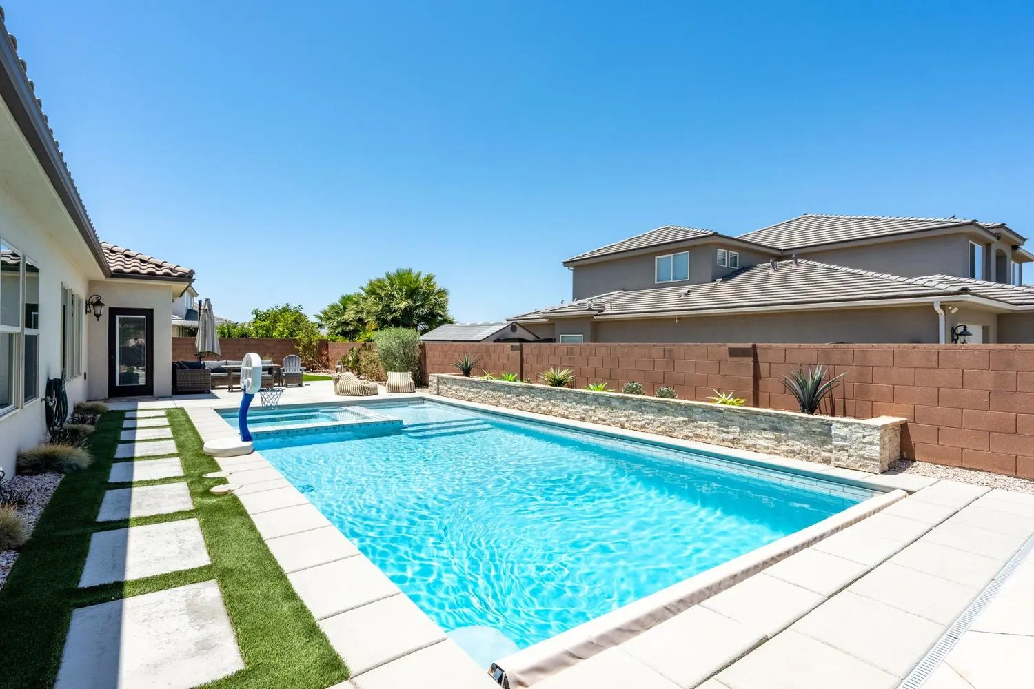 Backyard oasis featuring a sparkling rectangular pool, integrated spa, and an elevated planter with decorative stone