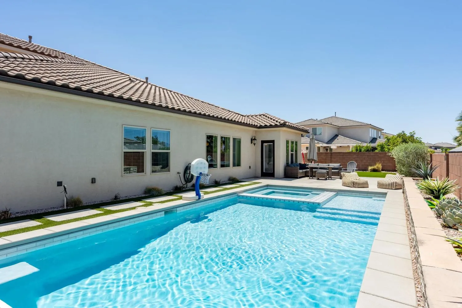 Outdoor living area featuring a rectangular pool with integrated spa, stucco exterior, tiled roof, and a paved patio space